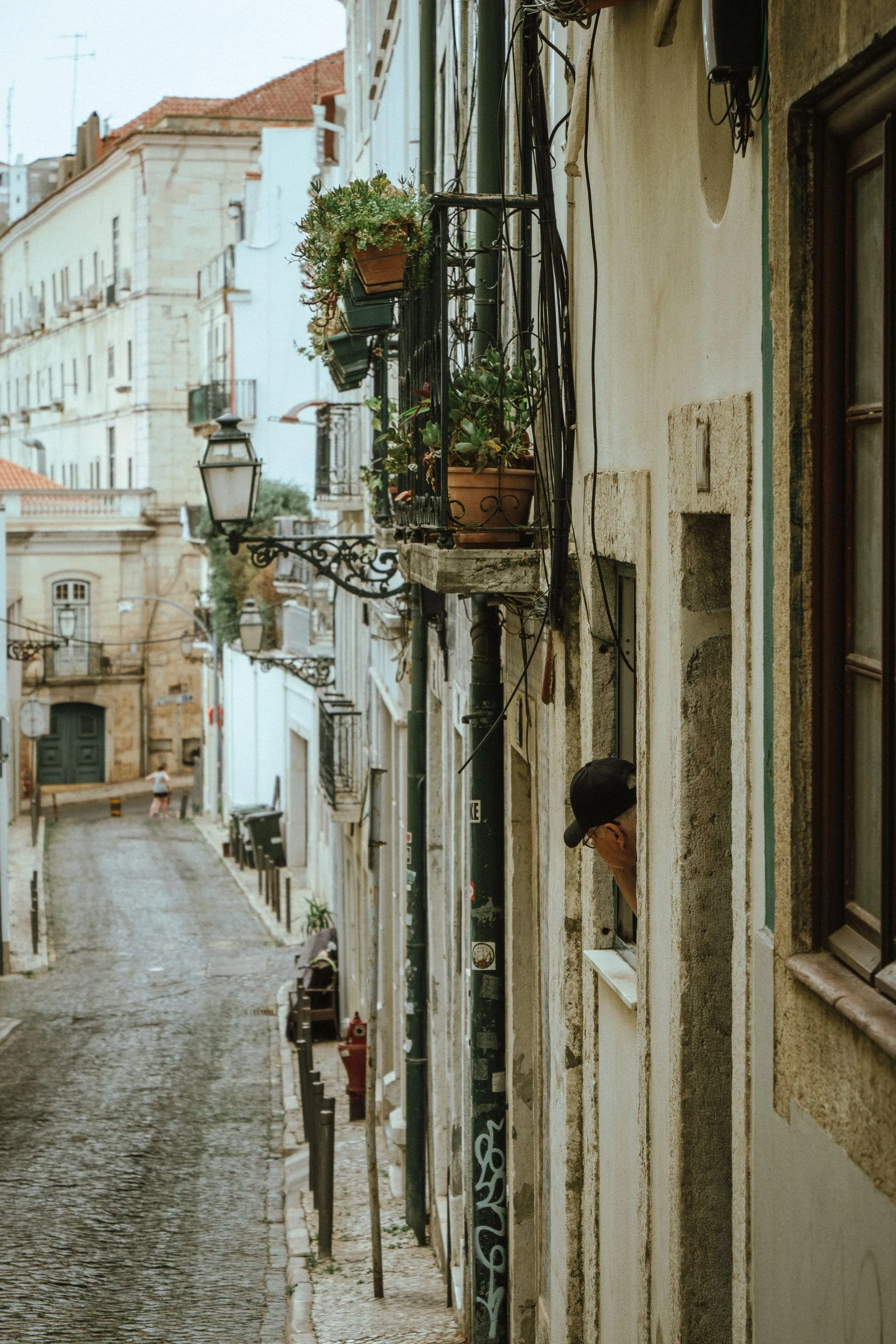 A narrow Lisbon street of tiled and painted facades with a balcony above