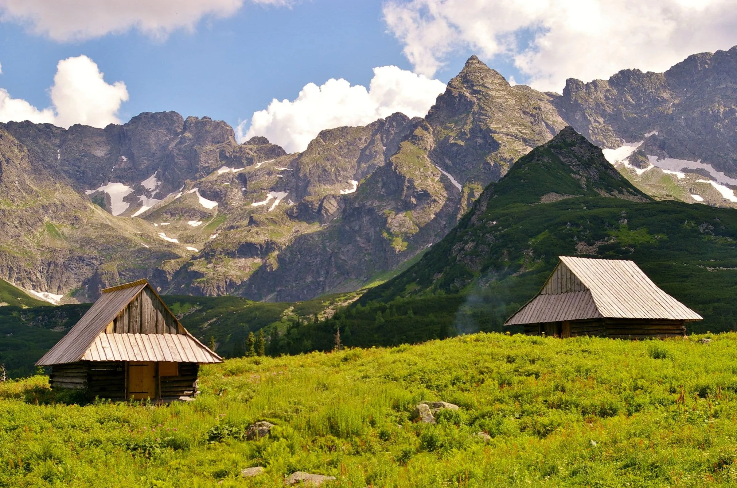 A wooden mountain hut on a green saddle below rocky peaks