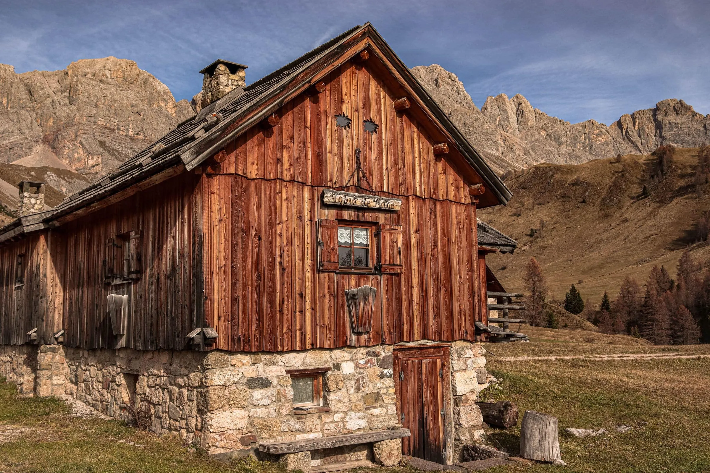A dark wooden cabin on a grass slope with mountains behind