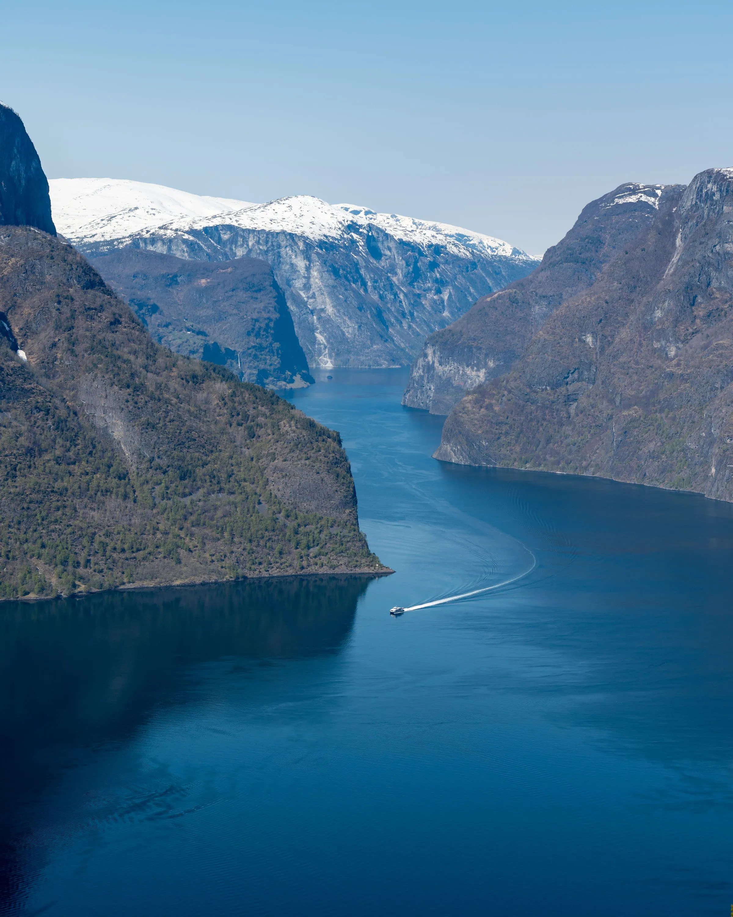 A ferry crossing a deep Norwegian fjord between steep grey cliffs
