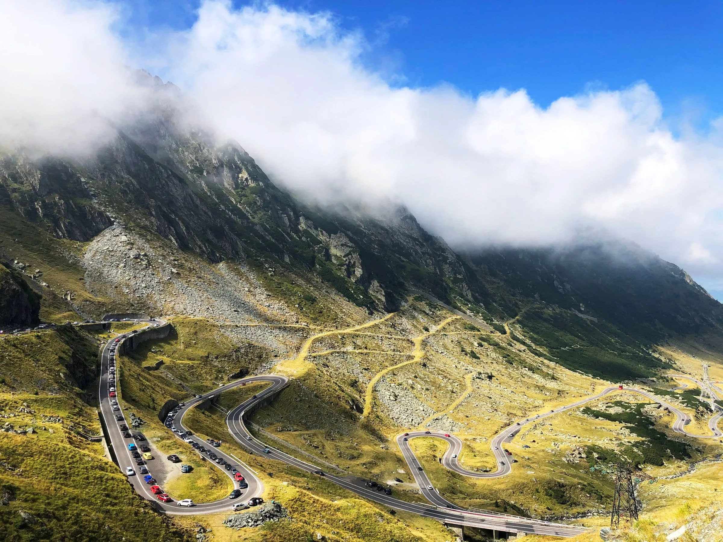 A mountain road switchbacking up a steep green slope in the sun