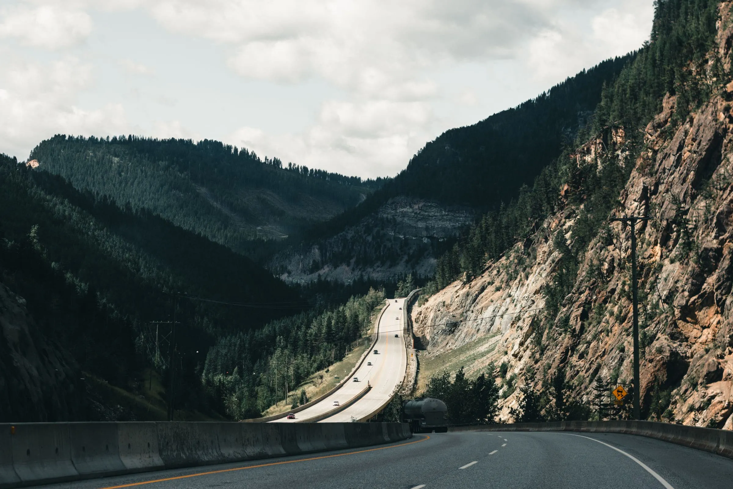 A road running below a huge dark cliff face beside water