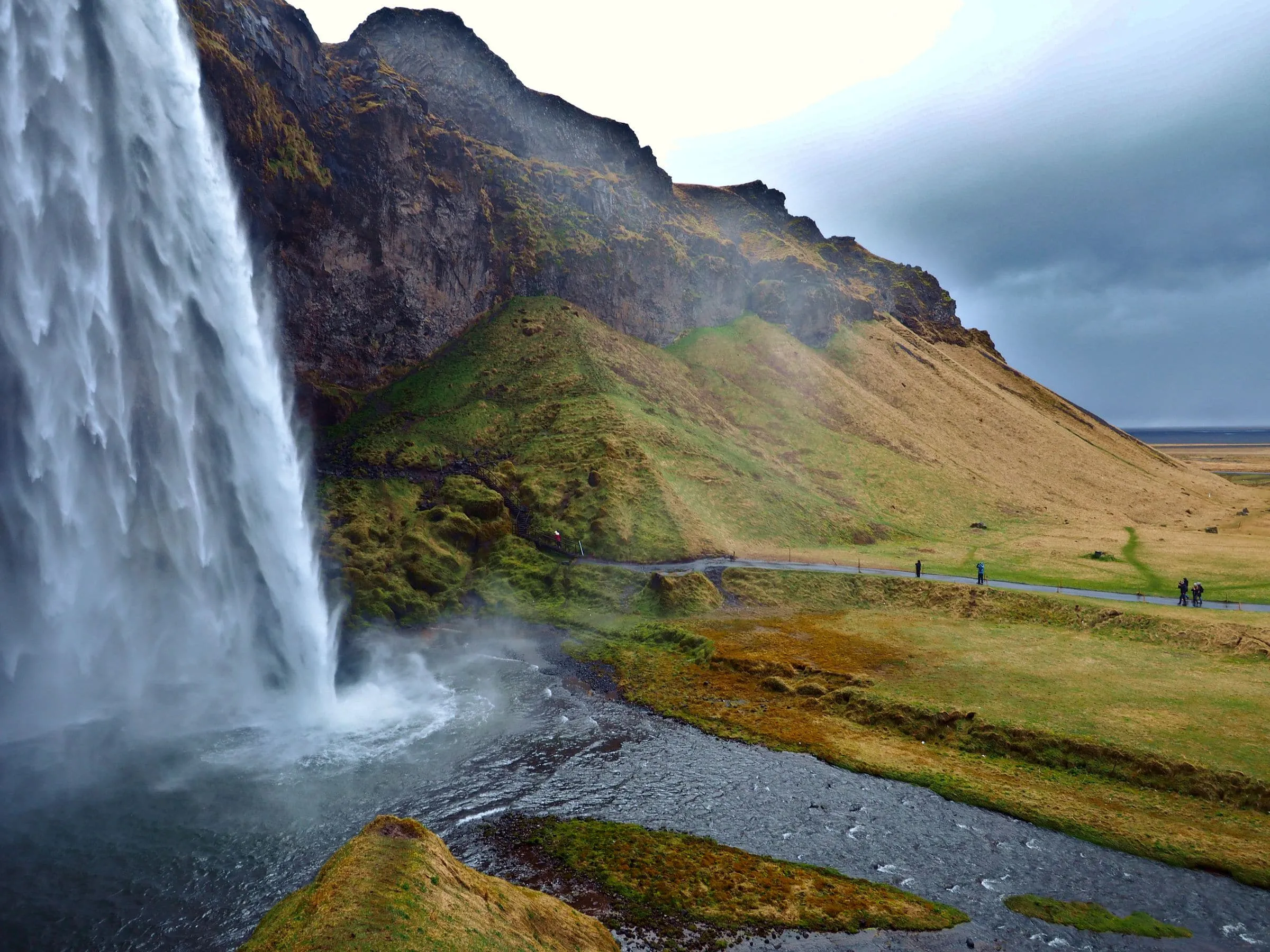 A tall waterfall falling over a green cliff with a path leading behind it