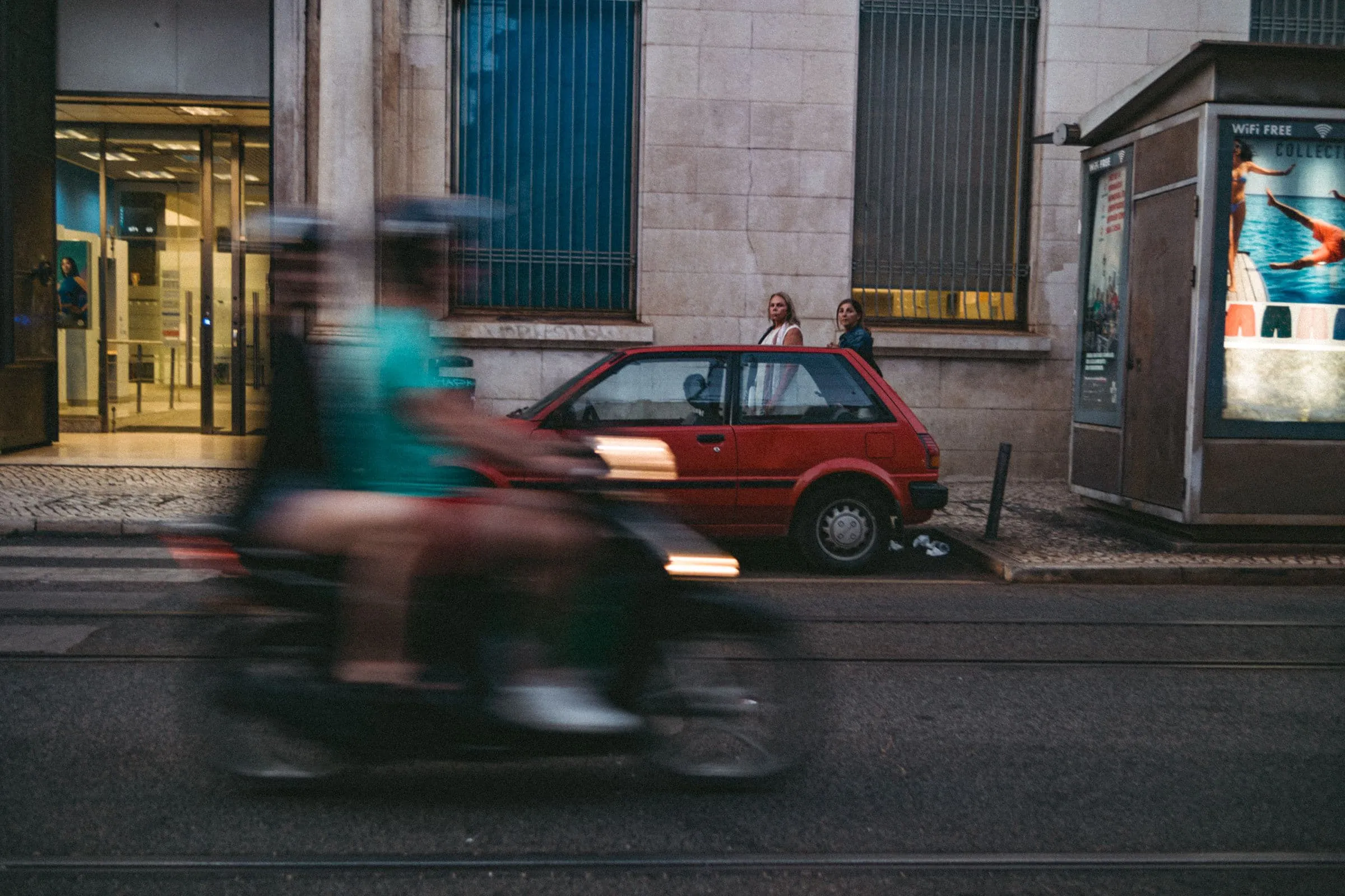 A motorcycle blurred with motion passing a parked car on a city street