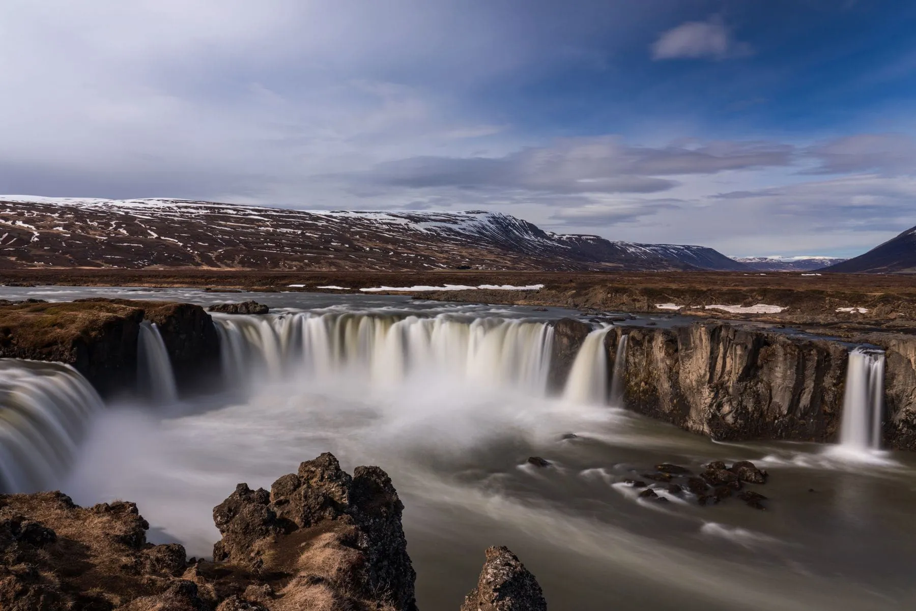 A wide waterfall spilling over a dark rock shelf into a pool