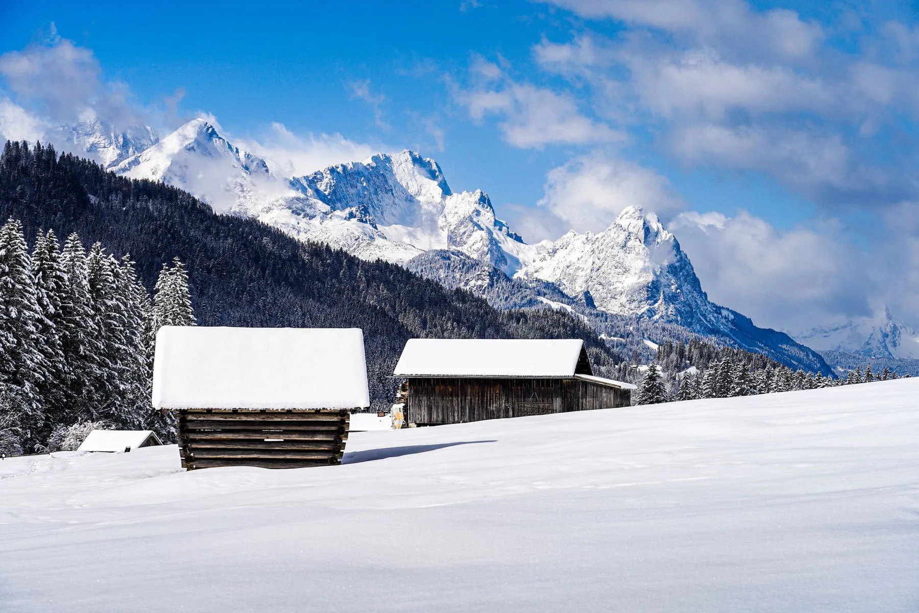 A small cabin in deep snow with mountains rising behind it