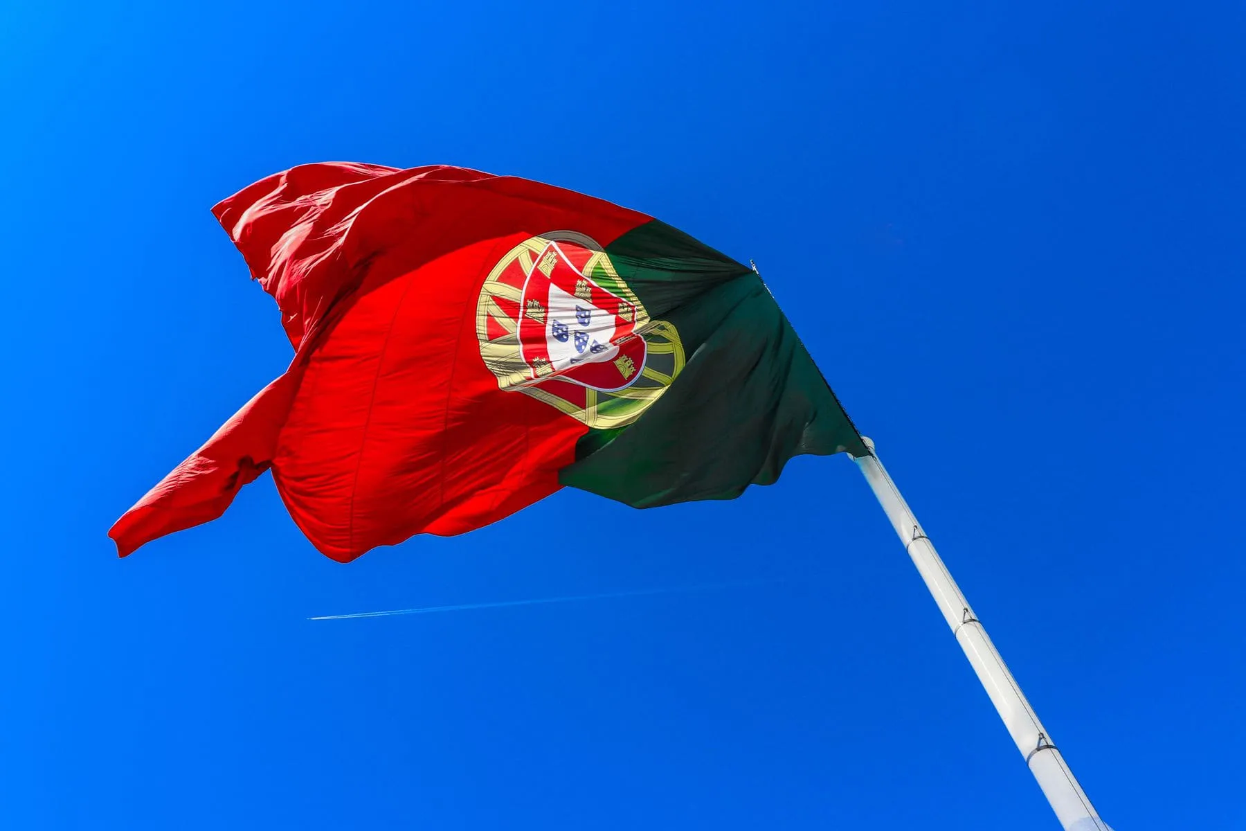 A Portuguese flag snapping in the wind against a deep blue sky
