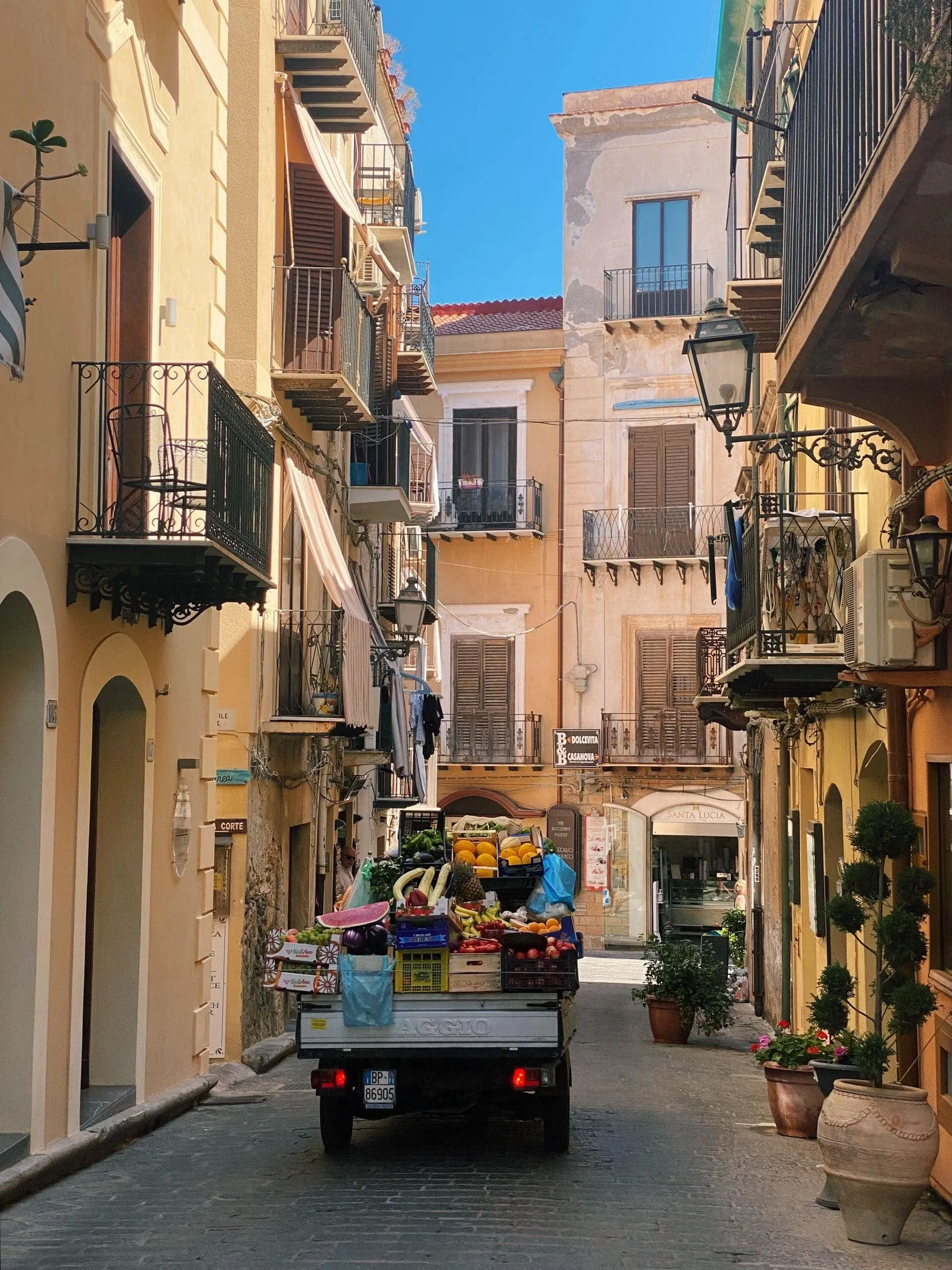 A street of balconied houses in a Sicilian town, shutters half closed against the sun