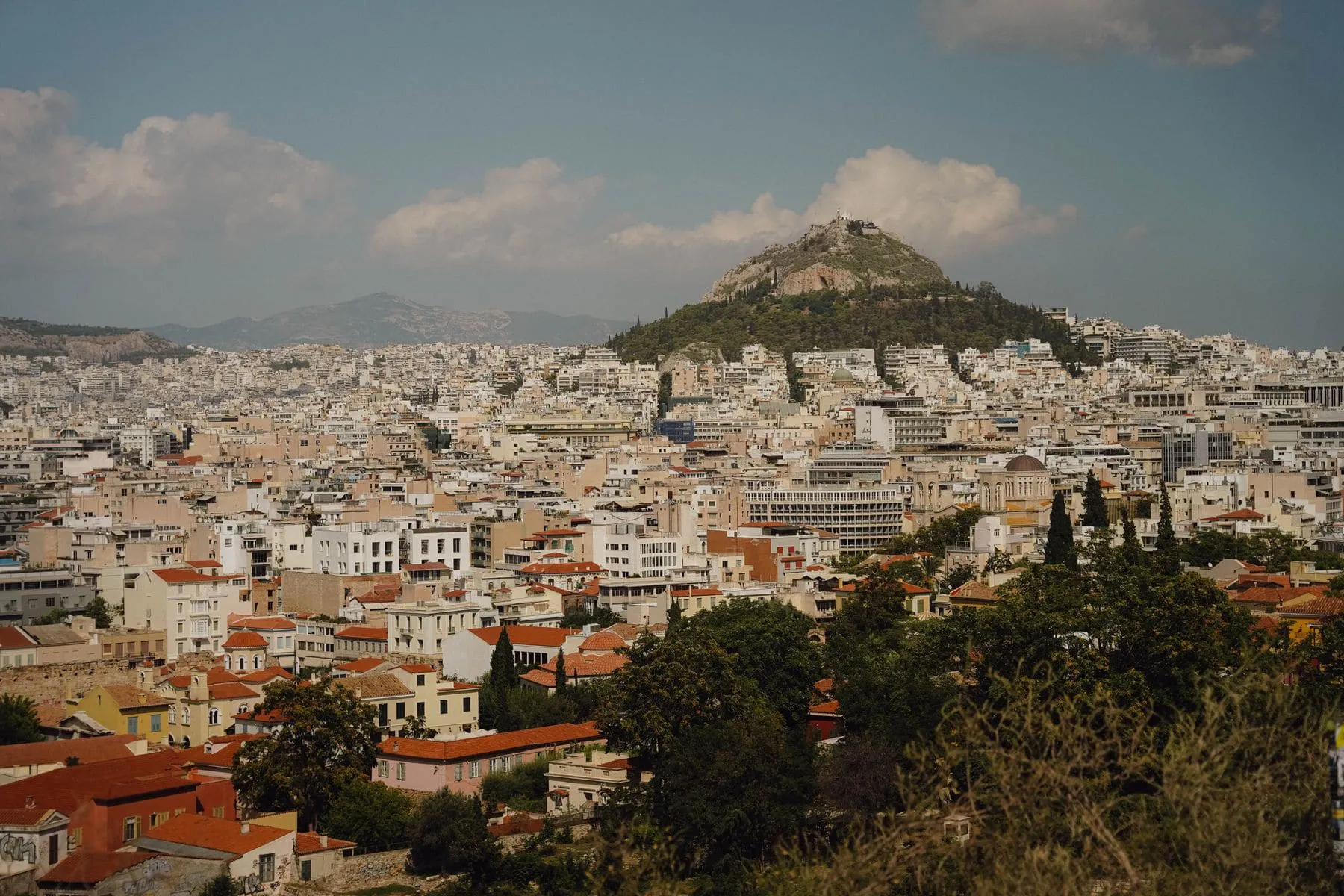 The city of Athens spread out below a green hill at dusk