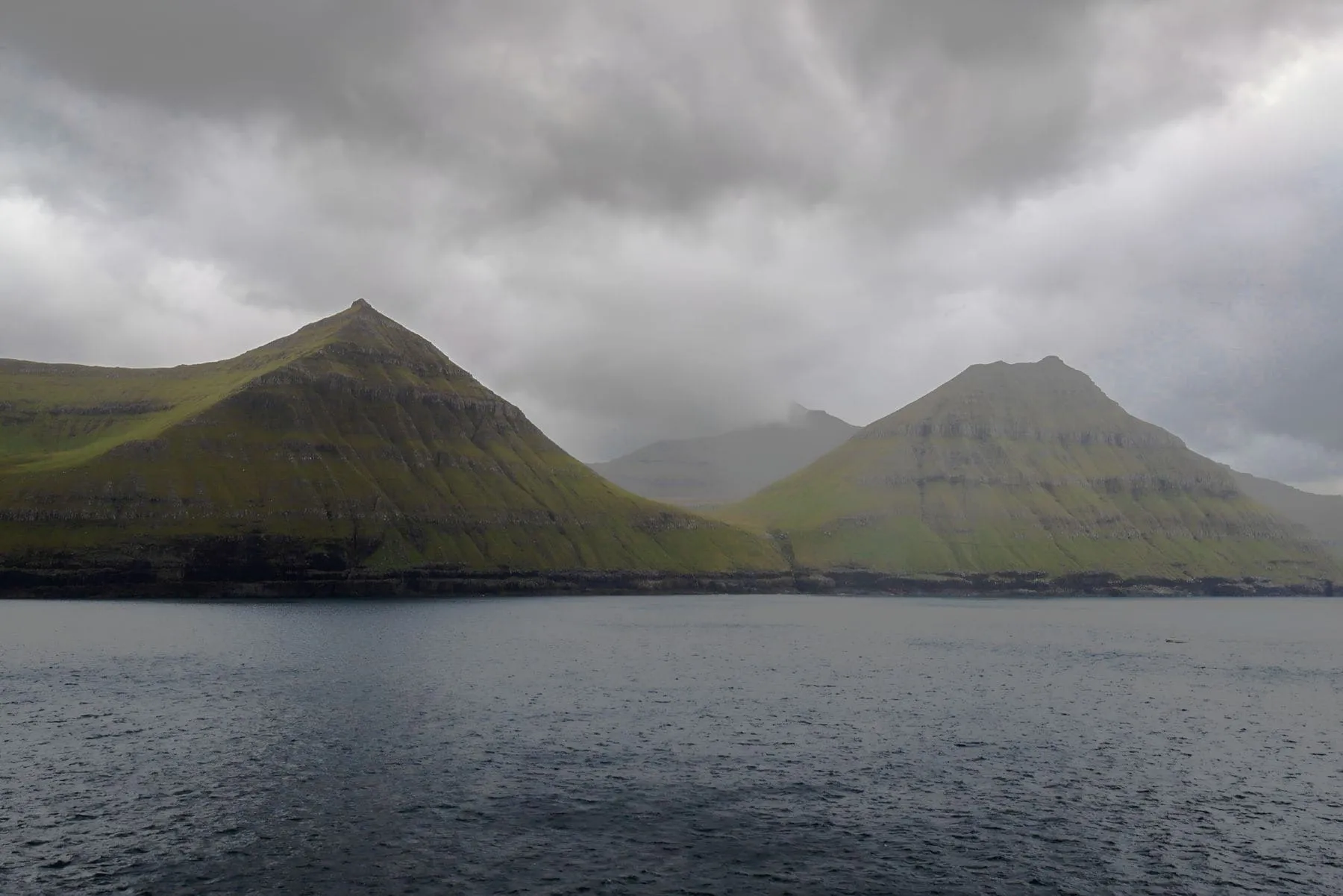 A steep-sided fjord between two green headlands under heavy cloud