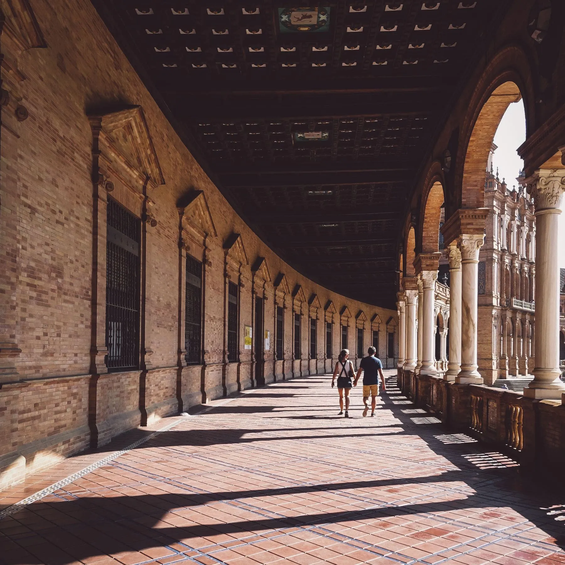 A long stone colonnade in Seville with figures walking through the shadows at the far end