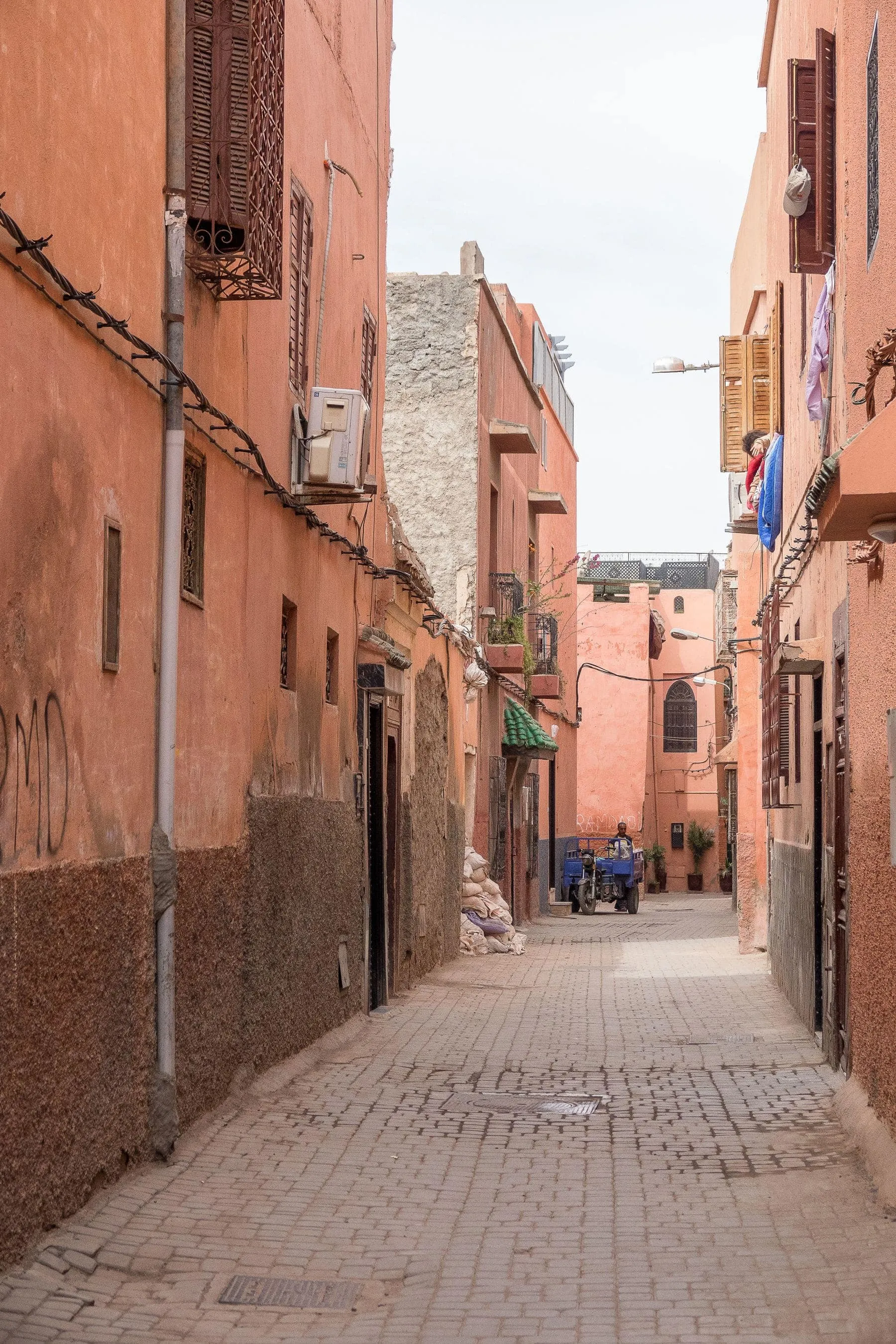 A narrow pink-walled alley in the Marrakech medina with figures at the far end