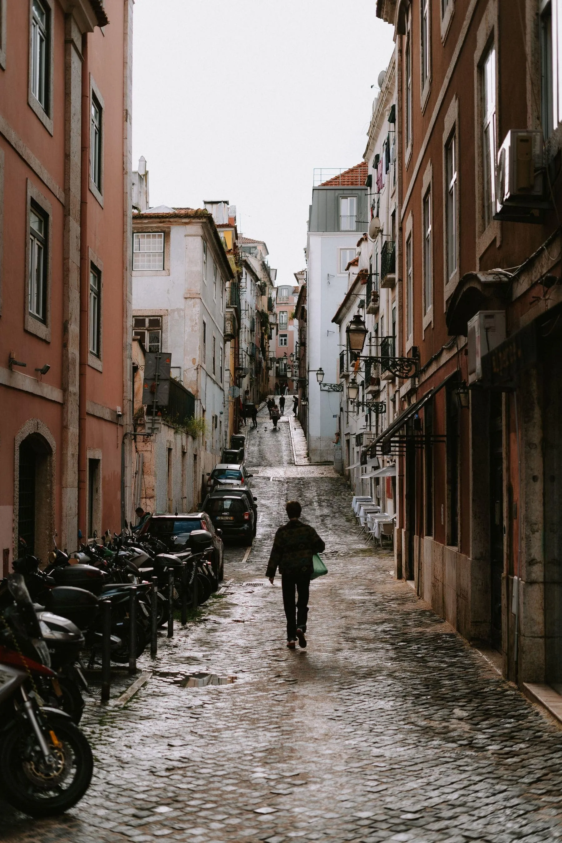 A narrow Lisbon street with cars parked on both sides and washing strung between balconies