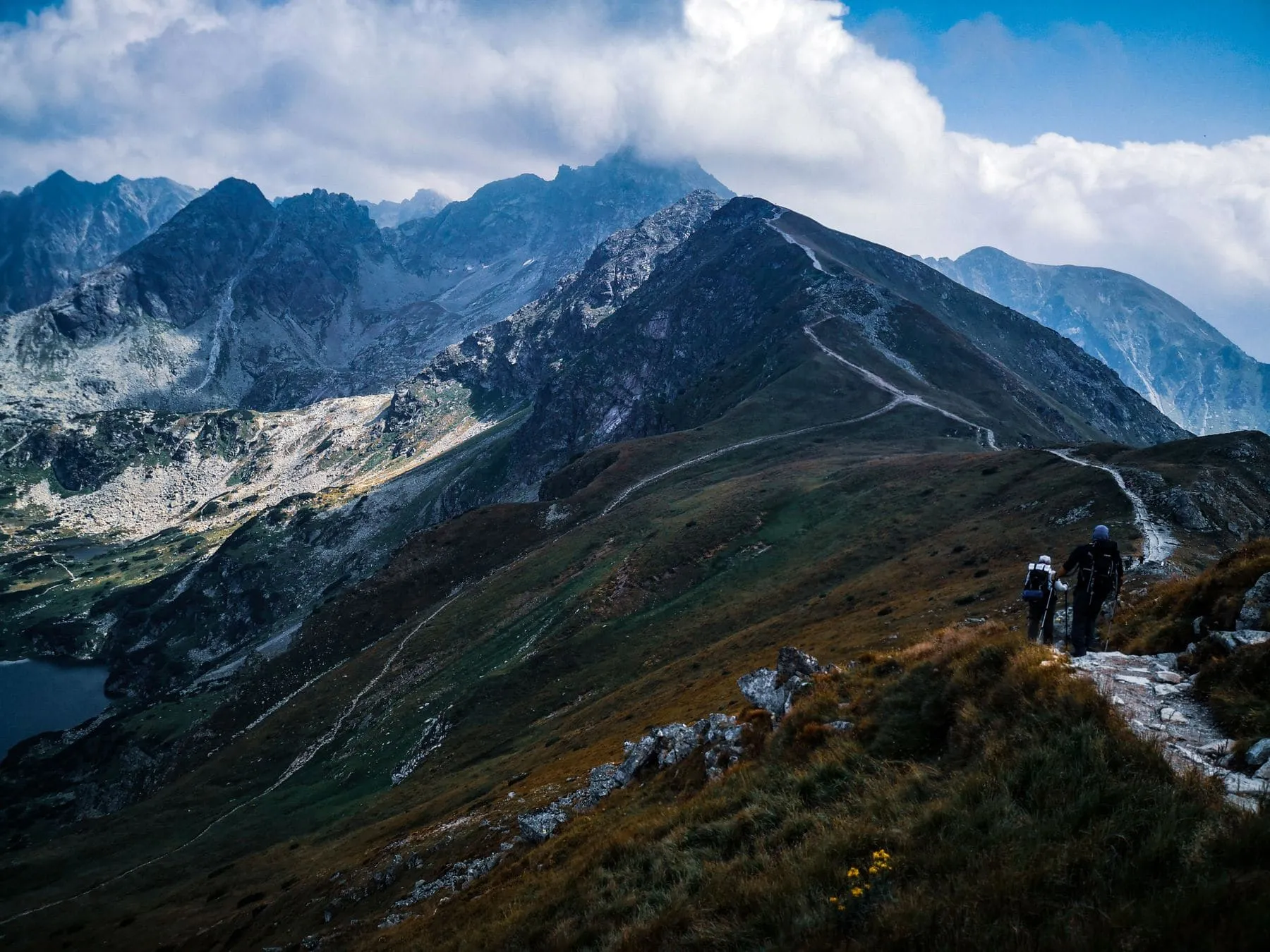 A path along a broad grassy ridge with mountains stacked behind