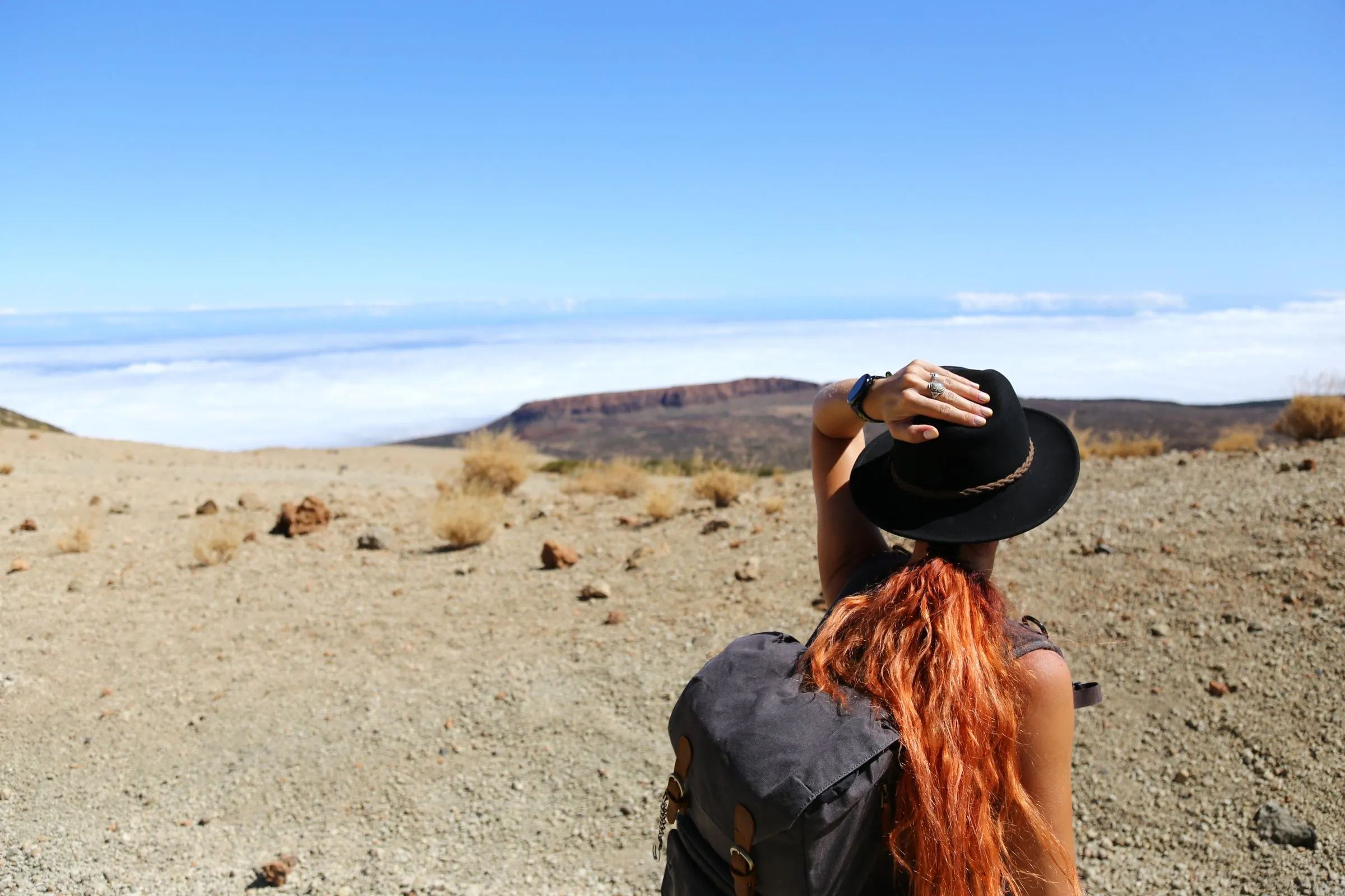 A traveller in a wide-brimmed hat and backpack looking out over a desert valley